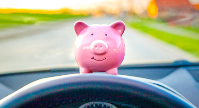 Piggy bank on dashboard of a car with stearing wheel partially in view